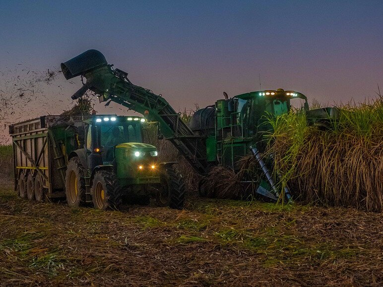 ein Traktor und Mähdrescher arbeiten im dunklen auf dem Feld